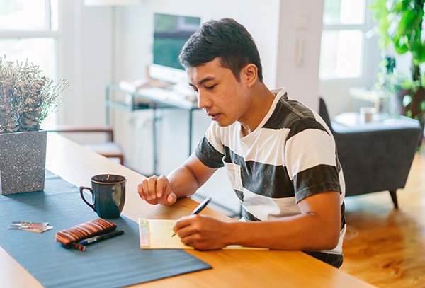 Young man writes on a notepad at table