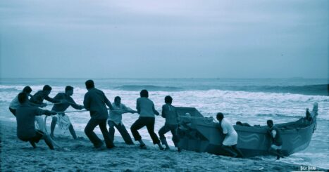 A group of men work together to pull a boat to shore on a sandy beach