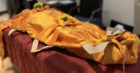 Dead woman wrapped in orange fabric with sunflowers and bows