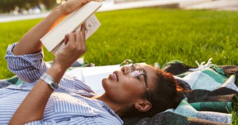 Young black woman reads a book on a blanket in a park