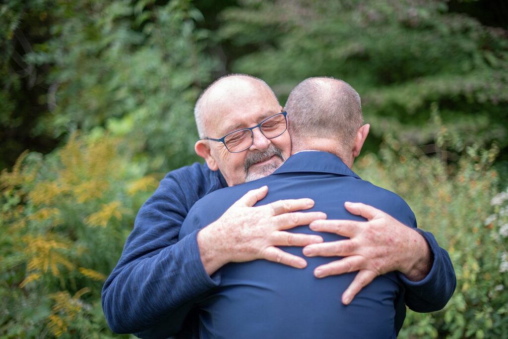 A married, elderly gay male couple embrace each other in a show of affection