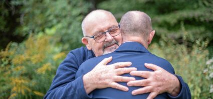 A married, elderly gay male couple embrace each other in a show of affection