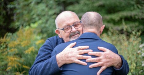 A married, elderly gay male couple embrace each other in a show of affection