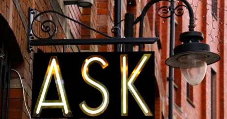 "ASK" neon sign beside streetlamp on brick street