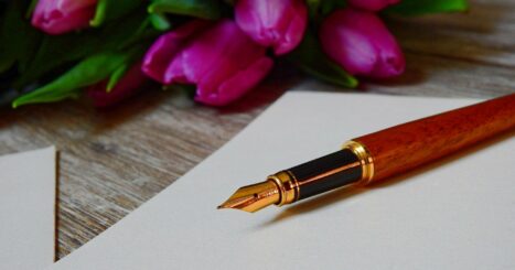 fountain pen on black sheet of paper next to bouquet of pink tulips